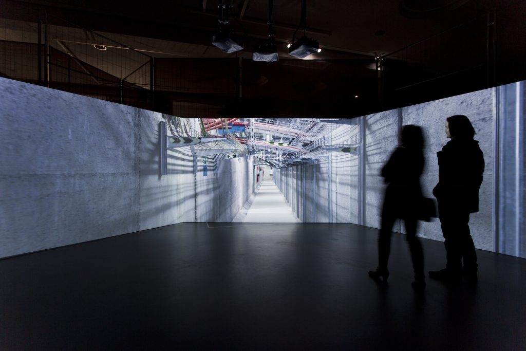 Three-screen installation view of Internet Machine at Transmediale 2015, a panoramic film of server rooms projected onto three large adjacent screens in a darkened gallery